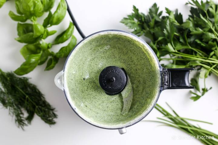 Blended green goddess dressing in a food processor with herbs on the side.