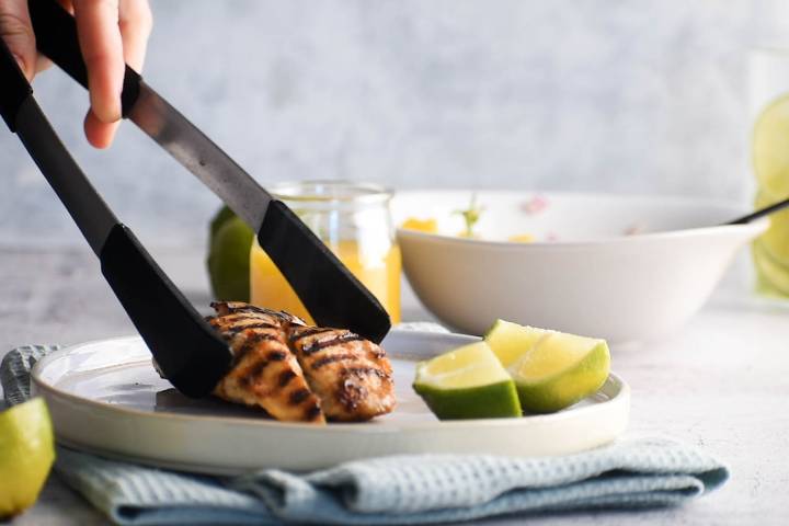 Grilled chicken breast on a plate with tongs.