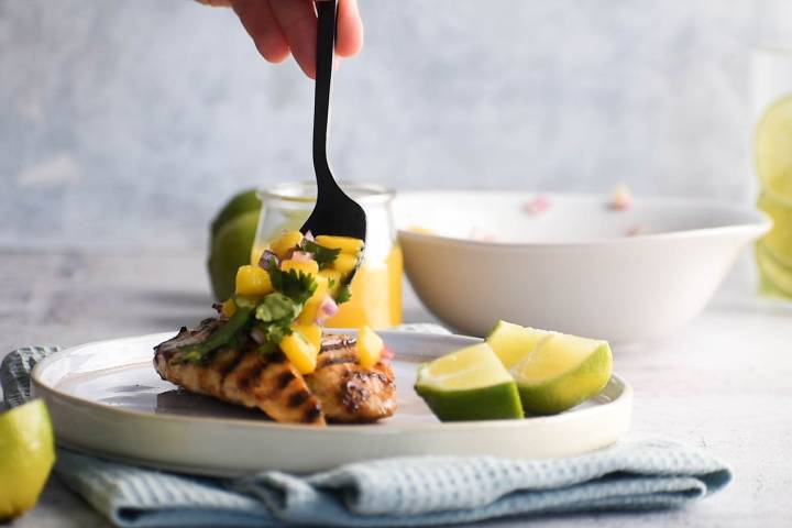 Mango salsa being served over grilled chicken breast.