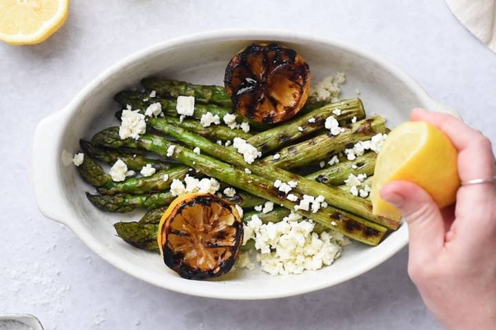 Lemon juice being squeezed over grilled asparagus.