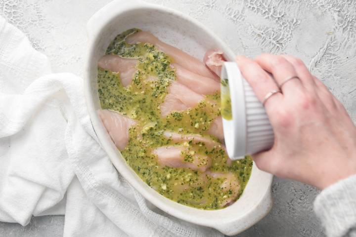 Chicken breast marinating in cilantro and lime sauce in a white dish.