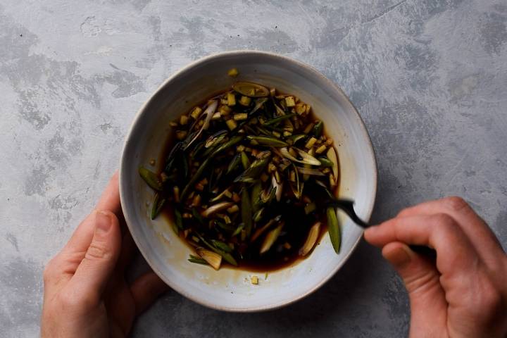 Soy sauce, green onions, garlic, ginger, and green onions being stirred in a bowl.