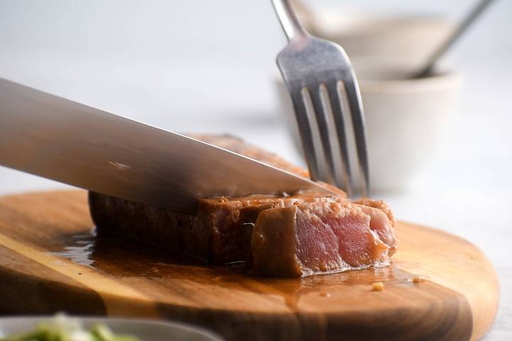 Grilled tuna being sliced on a wooden cutting board.