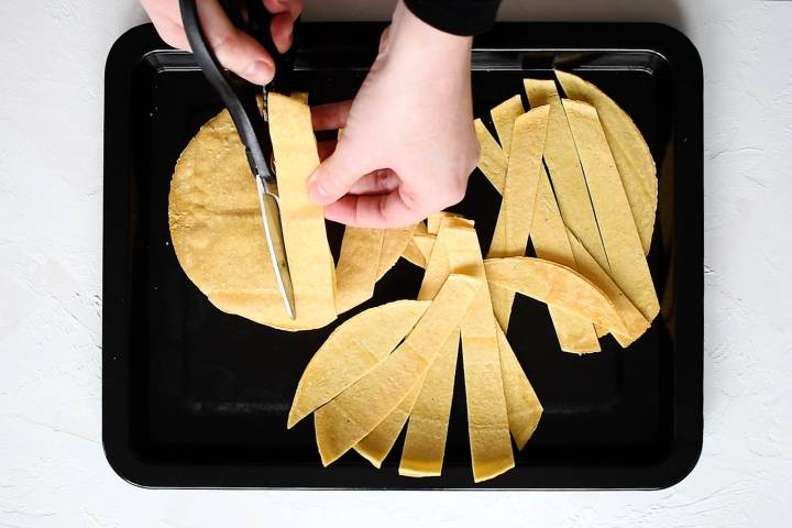 Corn tortillas being cut into strips and sprayed with cooking spray.