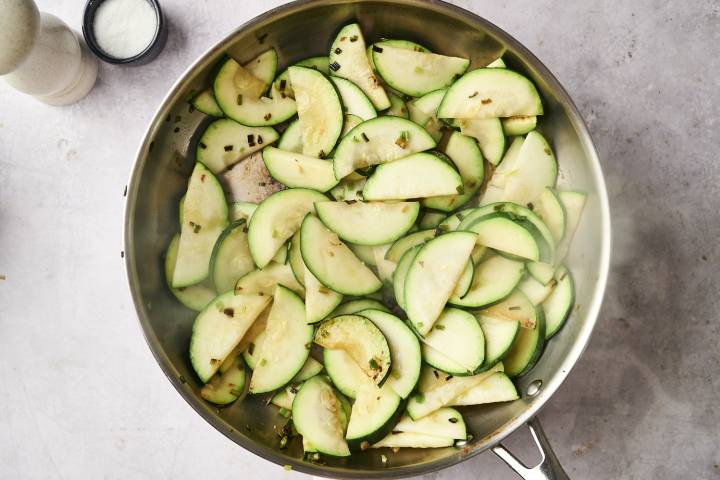 Sliced zucchini cooking in a stainless steel skillet, lightly sautéed with garlic and seasonings.
