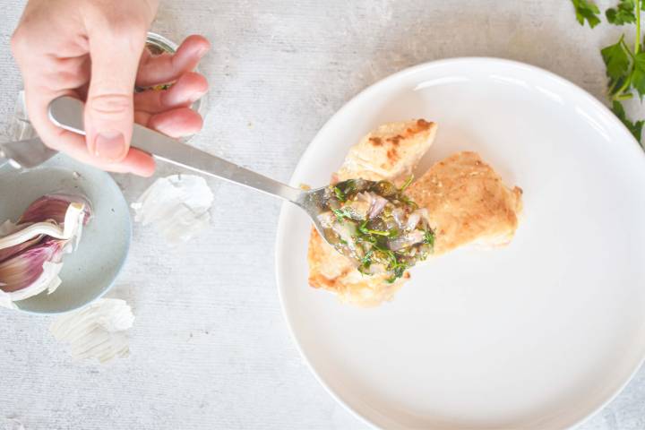 Chicken breast being served with piccata sauce on a plate. 