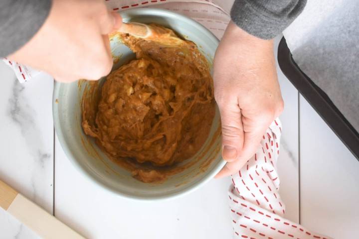 Peanut butter, banana, dates, vanilla extract, and spices being mixed in a bowl.