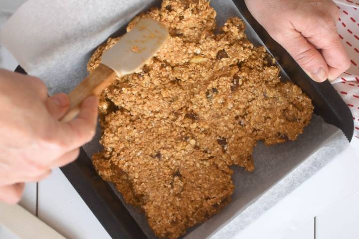 Oatmeal bar mixture being pressed into a baking sheet.