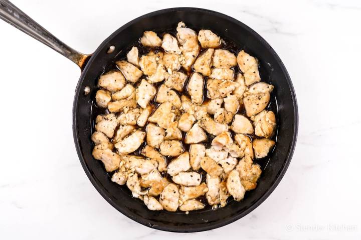Chicken breast tossed with sesame chicken sauce in a skillet.