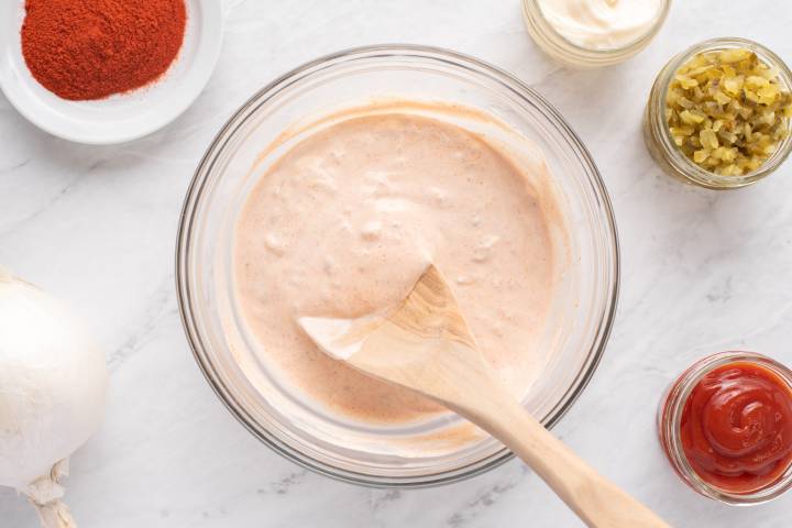 Ingredients for thousand island dressing being mixed in a glass bowl with a wooden spoon.