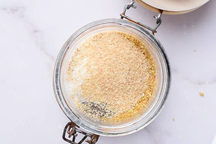 Garlic powder and onion powder being added to lemon zest and pepper in a jar.