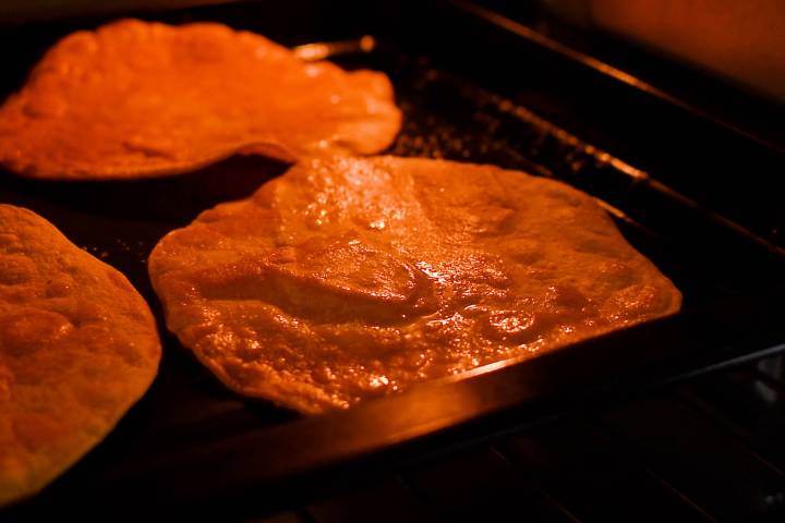 Tostada shells baking in the oven with small bubbles forming.