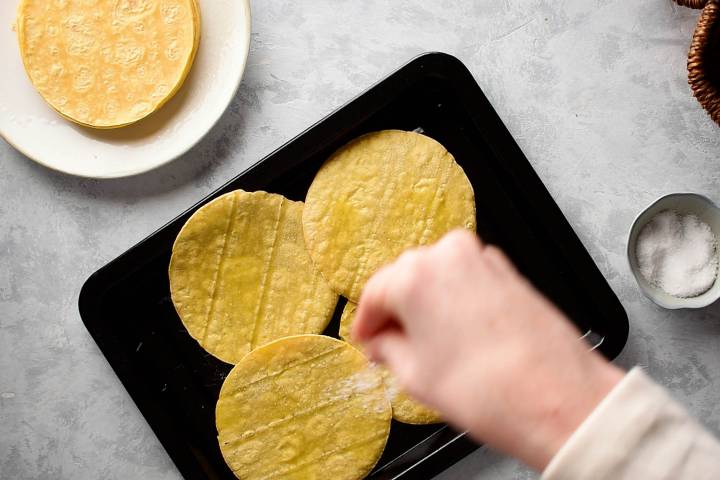 Corn tortillas being sprinkled with salt and pepper.