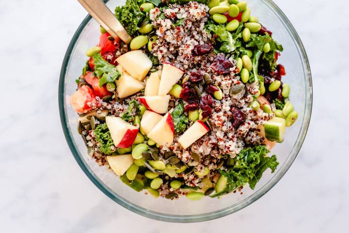 Kale, quinoa, apples, edamame, dried cranberries, and pumpkin seeds in a bowl.