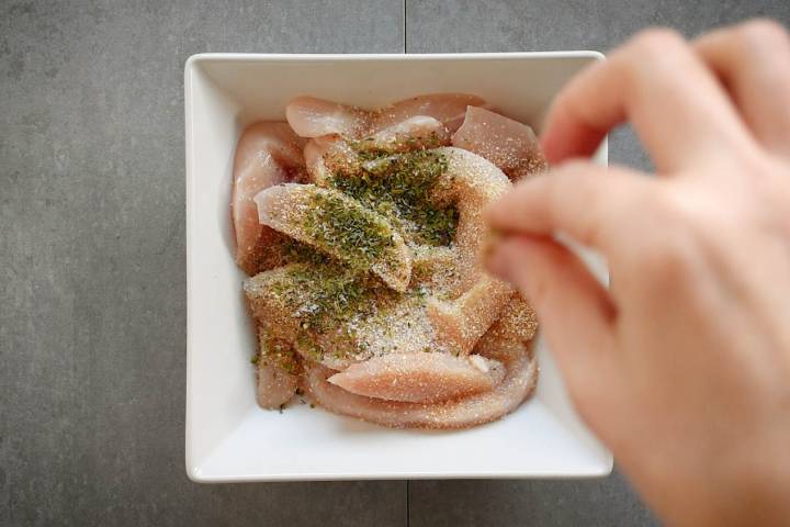 Chicken breast being seasoned with garlic powder, onion powder, salt, and pepper.