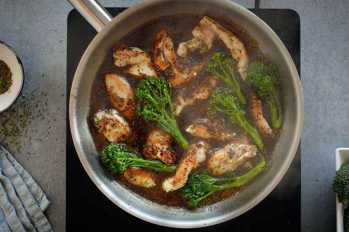 Honey mustard sauce being cooked in a pan with chicken breast and broccolini.
