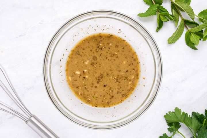 Homemade vinaigrette with olive oil, lemon juice, vinegar, and herbs in a bowl.