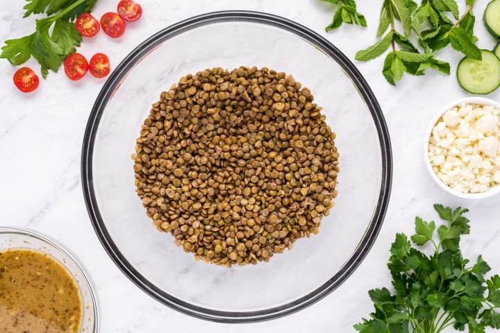 Cooked lentils in a bowl with herbs on the side.