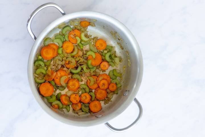 Carrot slices and celery pieces cooking in a large soup pot.
