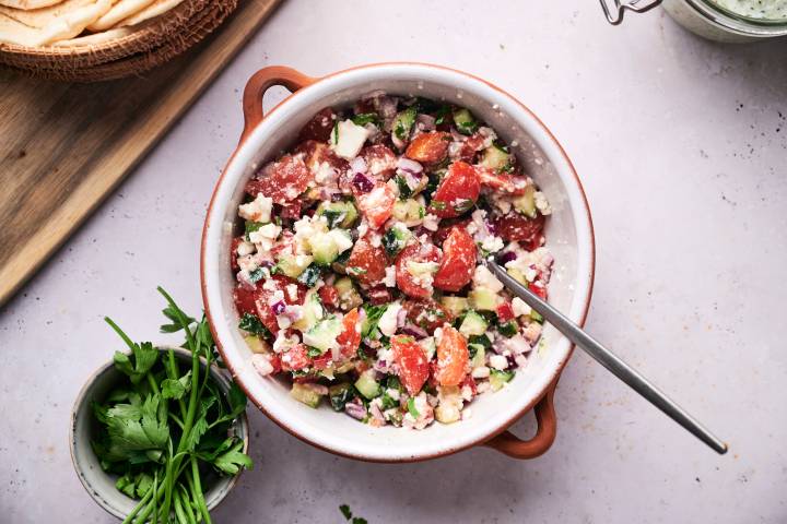 Cucumbers, tomatoes, bell pepper, red onion, parsley, and feta in a bowl.