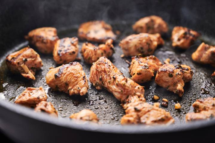 Mediterranean chicken pieces cooking in a skillet.