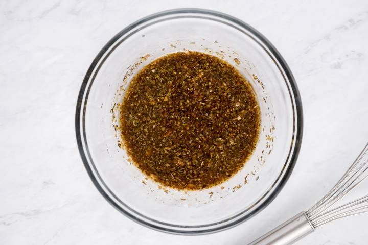 Olive oil, red wine vinegar, lemon juice, garlic, and oregano in a bowl.