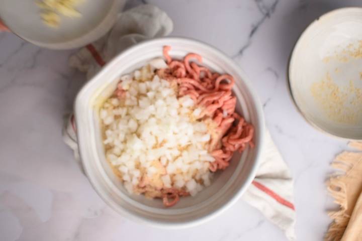 Ground beef, onions, garlic, and breadcrumbs in a bowl.