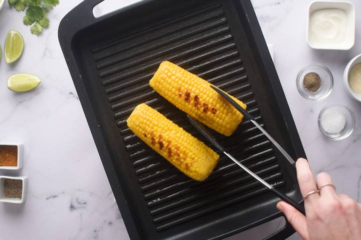 Corn on the cob cooking on a grill pan.