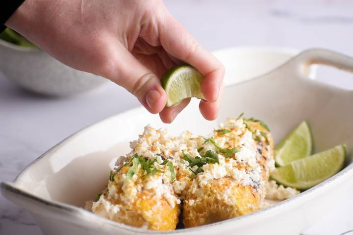 Lime juice being squeezed over Mexican street corn.