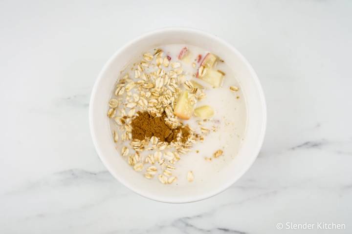 Oatmeal, cinnamon, maple syrup, almond milk, and apples in a bowl for oatmeal.