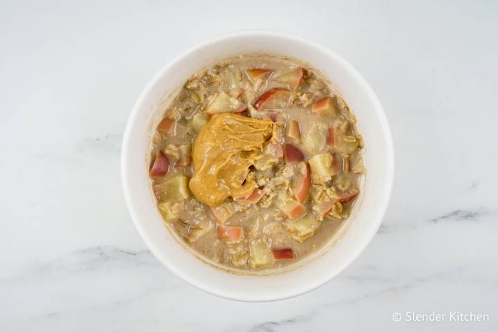 Cooked apple cinnamon oatmeal with a dollop of peanut butter in a bowl.
