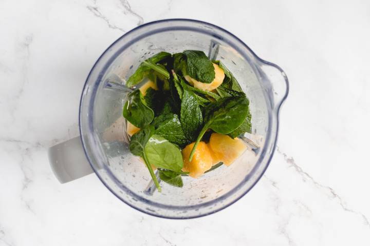 Fresh mint, spinach, and frozen pineapple in a blender.