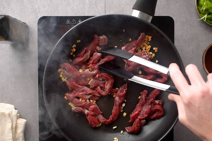 Thinly sliced beef cooking in a skillet with garlic and ginger.