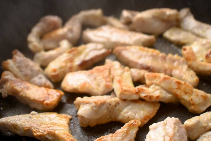 Thinly sliced pork tenderloin cooking in a skillet.