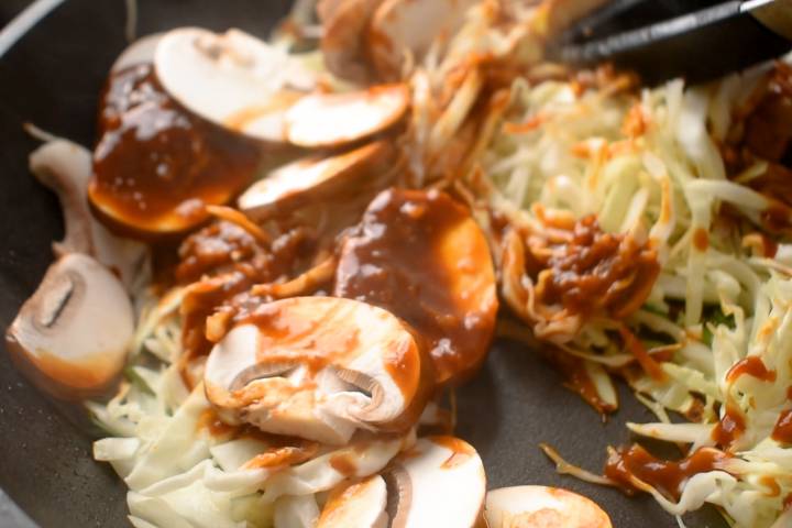 Mushrooms, carrots, scallions, and cabbage cooking in a skillet with moo shu sauce.