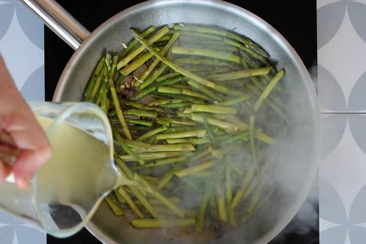 Asparagus cooking in a pan with chicken broth being poured over top.