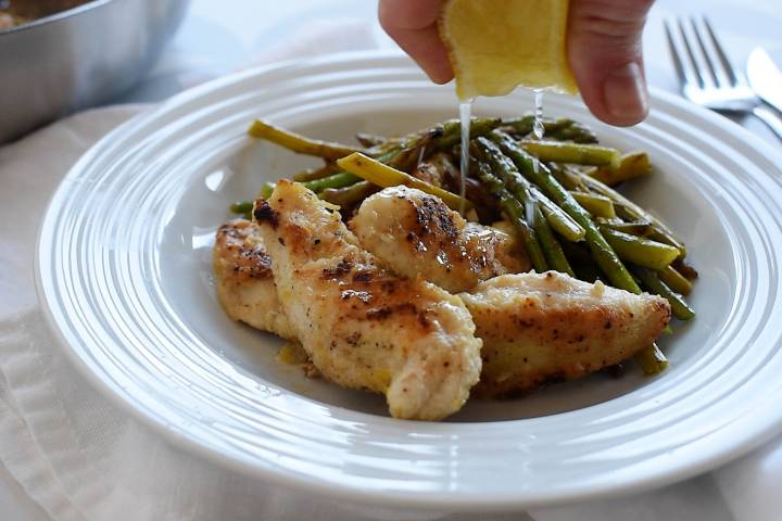 Lemon chicken served with asparagus with extra lemon being squeezed over top.