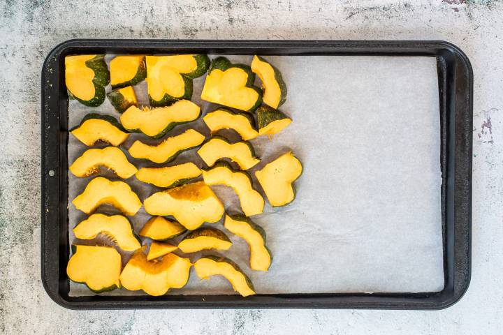 Sliced acorn squash on a sheet pan with parchment paper.