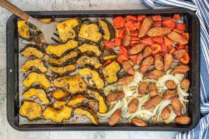 Roasted acorn squash, sausage, peppers, and onions on a sheet pan.
