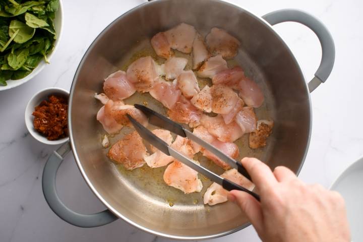Chicken breast cooking in a skillet with olive oil.