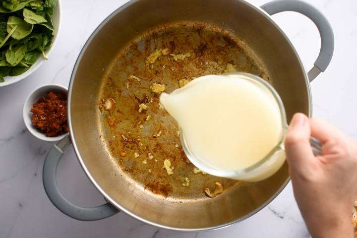 Chicken broth being added to a pan with sautéed garlic.