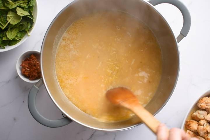 Orzo cooking in a pot with chicken broth.