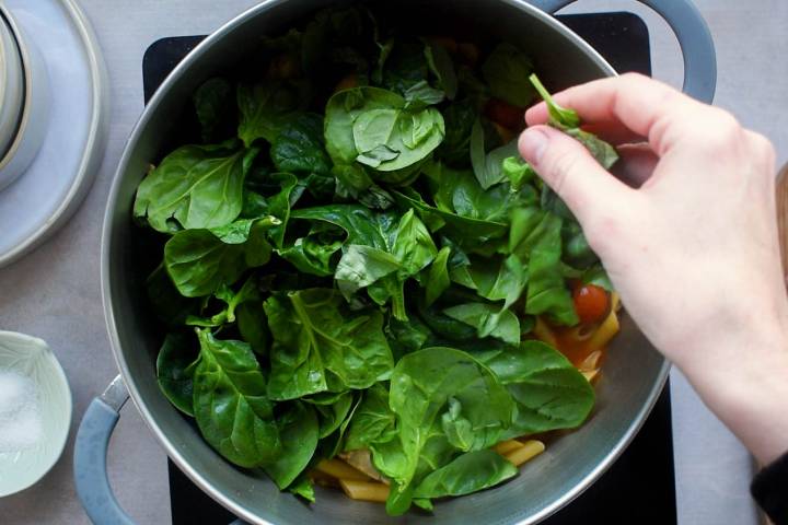 Spinach and basil being added to a pot of pasta.