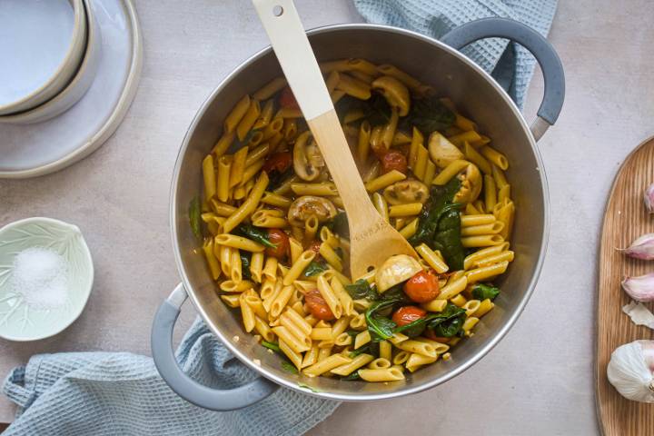 Cooked tomato and basil pasta with a wooden spoon.