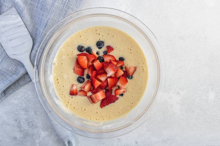 Muffin pancake batter with strawberries and blueberries in a glass bowl.