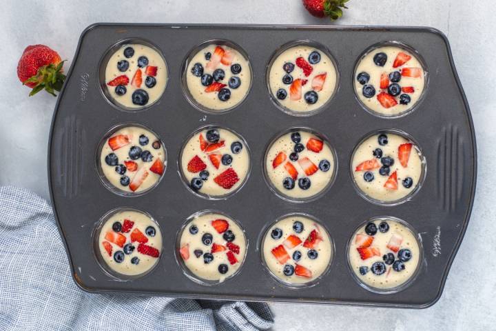 Pancake batter muffins in a tin with strawberries, blueberries, and bananas.