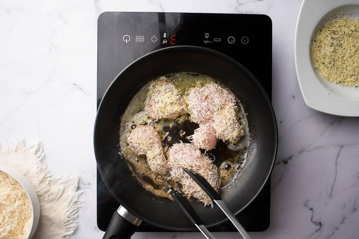 Parmesan chicken cutlets cooking in a pan with butter.