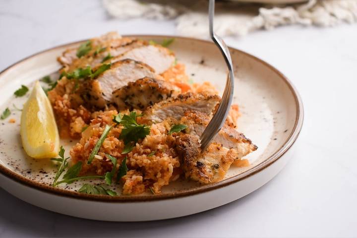 Sliced chicken breast served on a bed of parmesan garlic cauliflower rice.