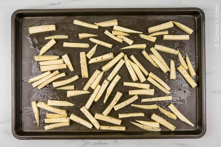 Parsnip fries in a single layer on a baking sheet.