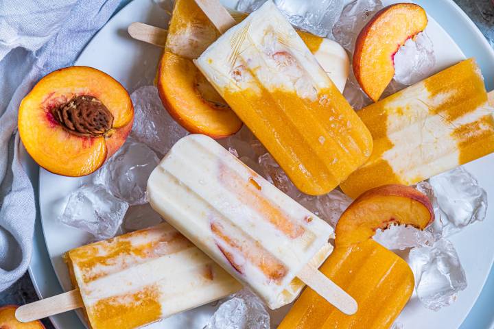 Peaches and cream popsicles on ice with fresh peaches.